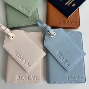 May include: A collection of four passport holders and matching luggage tags in sage green, tan, cream, and light blue. Each item features embossed names including ANA, JESSICA, ROSLYN, and TIARA. The tan holder displays a United States passport.