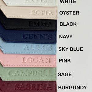 May include: A collection of personalized luggage tags in various colors, including gray, white, oyster, black, navy, sky blue, pink, sage, burgundy, and cognac. Each tag features a name embossed on the front.