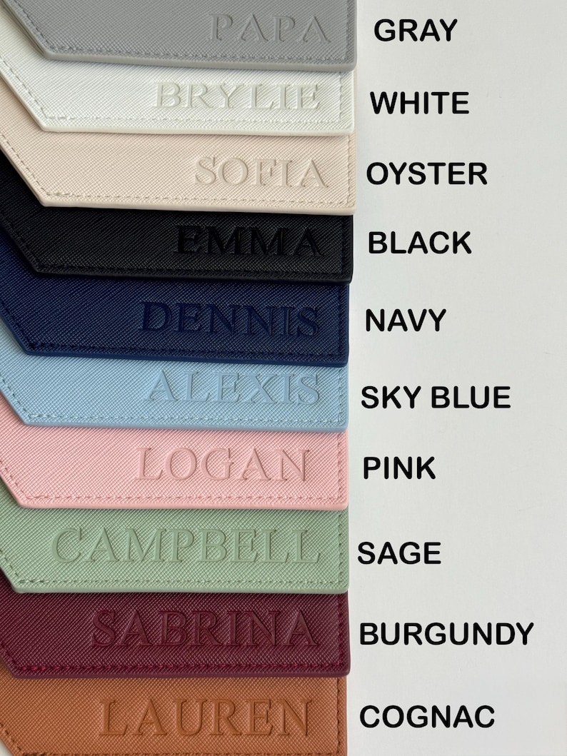 May include: A collection of personalized luggage tags in various colors, including gray, white, oyster, black, navy, sky blue, pink, sage, burgundy, and cognac. Each tag features a name embossed on the front.