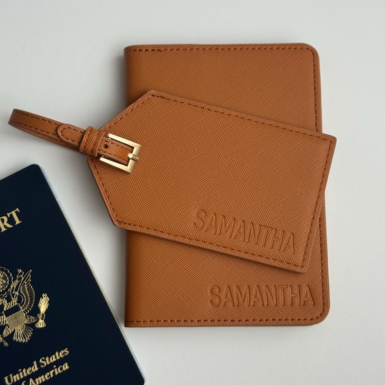 May include: A tan leather passport holder and luggage tag with the name "SAMANTHA" embossed on both. The luggage tag has a gold-colored buckle and strap. A blue United States passport is visible in the image.