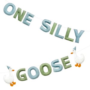 May include: A felt banner with the words "ONE SILLY GOOSE" in blue and green letters. Two white goose figures with party hats and orange feet are attached to the banner, creating a whimsical decoration.