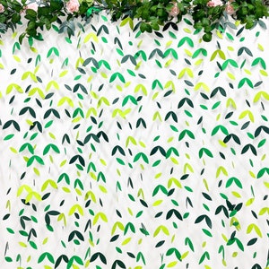 May include: A white background with green and yellow paper leaves hanging in a cascading pattern. The leaves are cut out in a simple leaf shape and are strung together on a clear string.