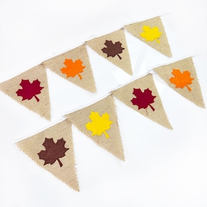 May include: A burlap banner with felt maple leaves in various colors, including red, orange, yellow, and brown. The banner is perfect for fall decorations.