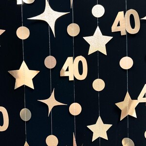 May include: Gold and white paper garland with stars, circles, and the number 40. The garland is perfect for a 40th birthday party.