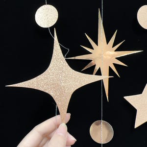 May include: A garland of gold glitter stars and circles, perfect for a party or special occasion. The garland is made of paper and is strung together with twine.