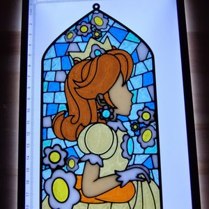 May include: A stained glass window featuring a princess with a crown and a yellow dress. The princess is surrounded by blue and white flowers. The window is framed in black and is approximately 19 inches tall.