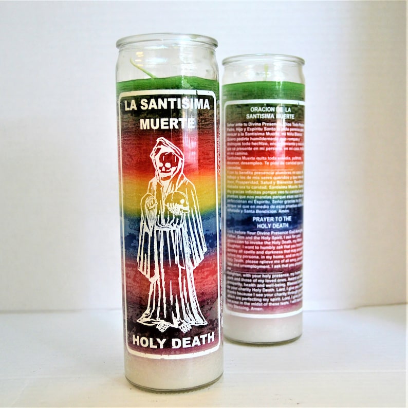 May include: Two glass candle jars with a rainbow colored design and a white image of a skeleton figure wearing a robe and holding a skull. The text "La Santisima Muerte" and "Holy Death" are printed on the jars.