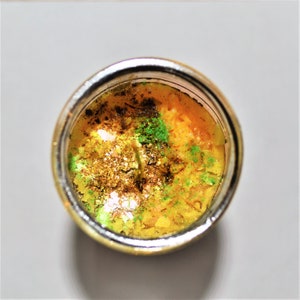 May include: A yellow candle with green and brown flecks in a clear glass jar with a silver rim.