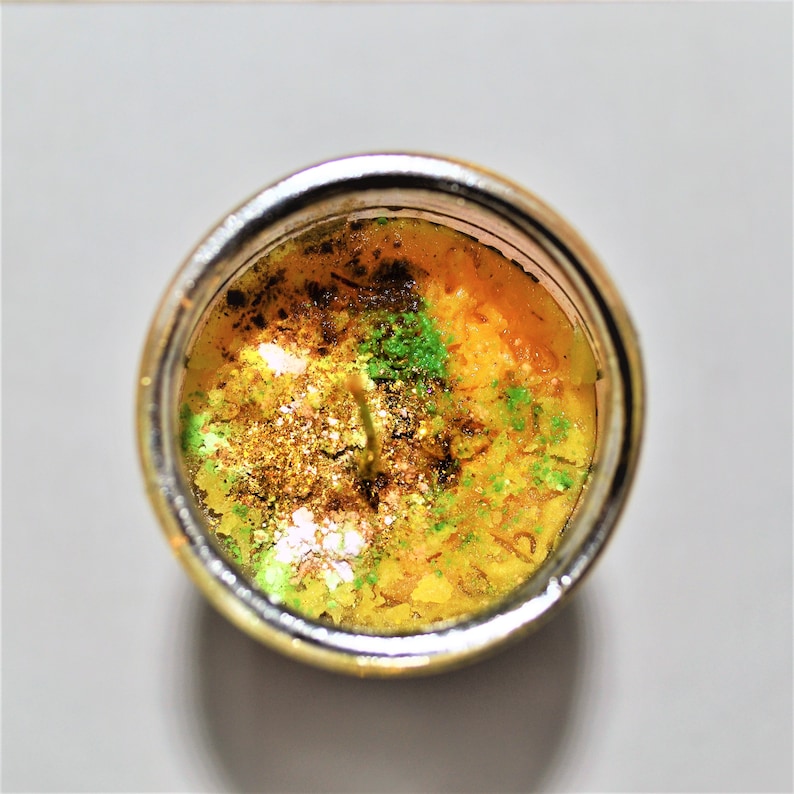 May include: A yellow candle with green and brown flecks in a clear glass jar with a silver rim.