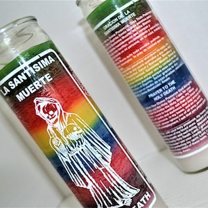 May include: Two glass candle jars with rainbow colored wax and white labels. The label on the left jar reads "La Santisima Muerte" and the label on the right jar reads "Oracion de la Santisima Muerte" and "Prayer to the Holy Death".