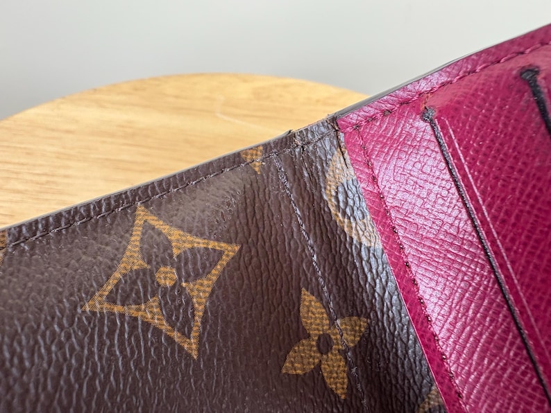 May include: Close-up of a brown leather wallet with a burgundy interior. The wallet features the iconic brown monogram pattern with the interlocking LV logo. The interior has card slots and a smooth, textured finish.