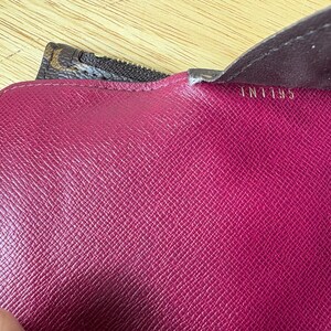 May include: Close-up of a magenta leather wallet interior. The wallet has a textured surface and the text "IN1195" is visible. A brown and tan patterned zipper is partially visible.