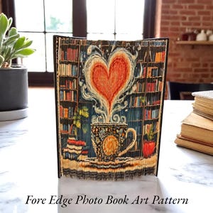 May include: A folded book art piece featuring a coffee cup design with steam rising into a heart shape. The background depicts bookshelves. The text "Fore Edge Photo Book Art Pattern" and "CreationsByCasady" are visible.