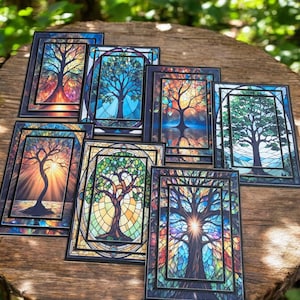May include: Eight colorful stained glass tree art prints with black frames. The trees are depicted in various styles and colors, including blue, green, red, orange, and purple.