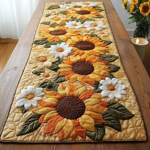 Puede incluir: Camino de mesa acolchado con un patrón repetido de girasoles y margaritas blancas. Los girasoles tienen centros marrones y pétalos en tonos de amarillo y naranja. Hojas verdes y un fondo amarillo claro completan el diseño.