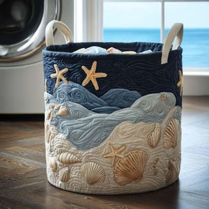 May include: A round, quilted laundry hamper with a coastal theme. The design features embroidered seashells, starfish, and ocean waves in shades of blue, beige, and tan. The hamper has two white fabric handles and is filled with laundry.