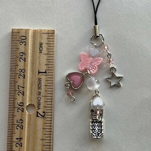 May include: A pink and white butterfly charm with a silver heart, star, and phone charm. The charms are attached to a black string with a silver clasp.