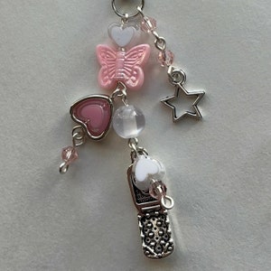 May include: A silver charm with a pink butterfly, pink heart, white heart, clear bead, silver star, and a silver flip phone charm.