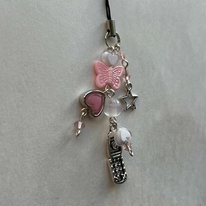 May include: A silver charm phone with pink and white hearts, a butterfly, a star, and clear beads on a black string.