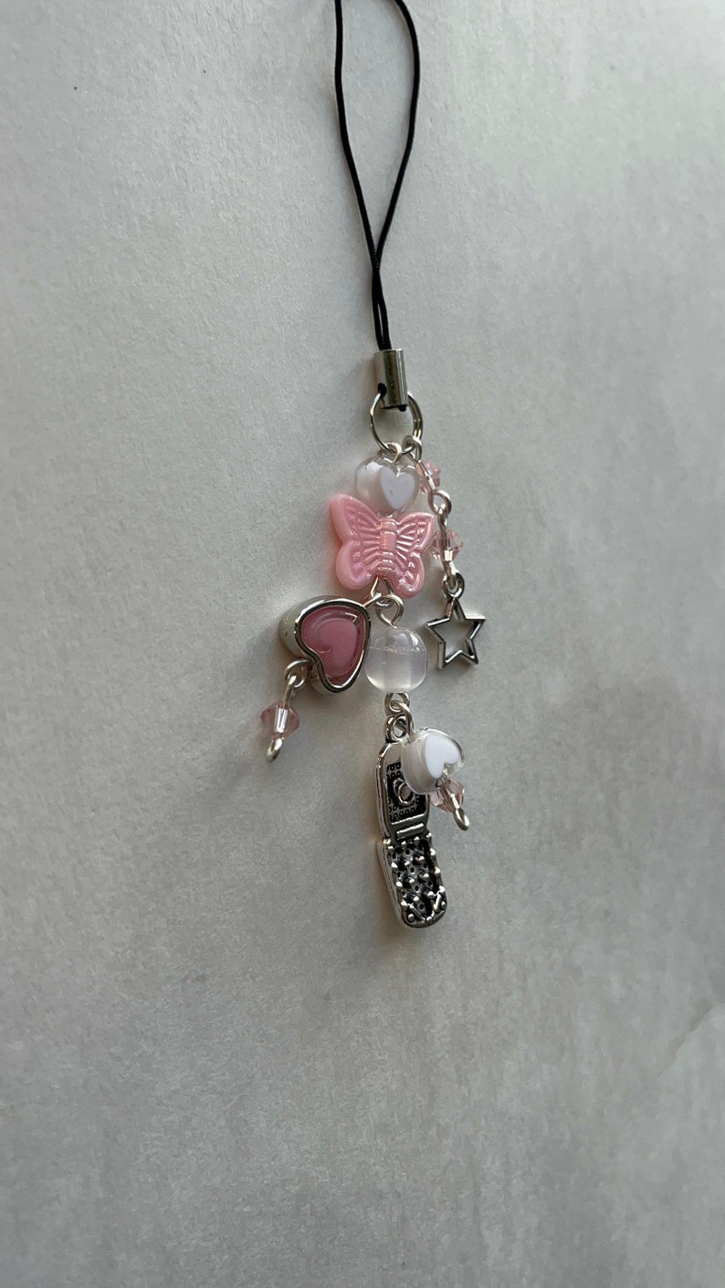 May include: A silver charm phone with pink and white hearts, a butterfly, a star, and clear beads on a black string.