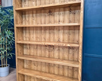May include: A tall, rectangular wooden bookcase featuring a natural light brown wood grain finish. The unit consists of five horizontal shelves and a vertical planked back panel, providing an open storage structure with a clear, polished wood texture.