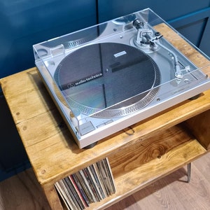 May include: A silver Audio-Technica turntable with a clear plastic dust cover, a circular black platter, and a silver tonearm assembly. The device features a metallic finish, visible control buttons, and the brand name printed on the platter.