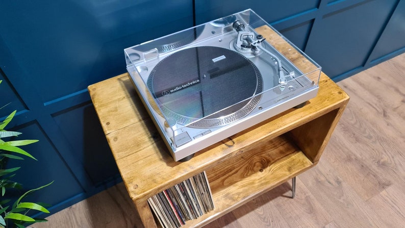 May include: A silver Audio-Technica turntable with a clear plastic dust cover, a circular black platter, and a silver tonearm assembly. The device features a metallic finish, visible control buttons, and the brand name printed on the platter.