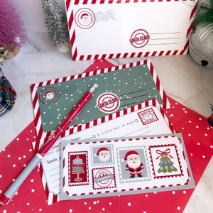 May include: A festive Christmas stationery set featuring envelopes, cards, and a pen. The envelopes are white with red stripes and a Santa Claus stamp. The cards have a green background with a Santa Claus stamp and a North Pole stamp.
