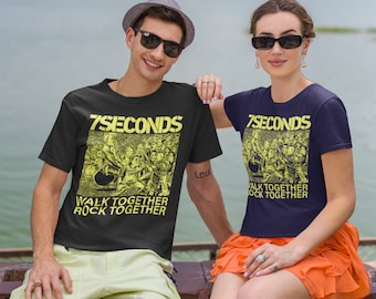 May include: A couple wearing matching black t-shirts with a yellow graphic of a band called "7 Seconds" and the text "Walk Together Rock Together". The man is wearing a brown hat and sunglasses. The woman is wearing a bright orange skirt.