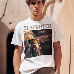 May include: White t-shirt with a graphic print of a woman standing in front of a carnival ride. The text "SLAUGHTER" is printed in gold letters above the graphic.
