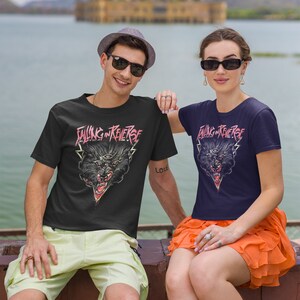 May include: Two people wearing black and navy blue t-shirts with a black wolf graphic and the text "Falling in Reverse". The man is wearing a grey hat and the woman is wearing a bright orange skirt.
