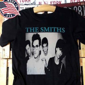May include: Black t-shirt with a graphic print of a band, The Smiths. The band members are in black and white, and the band name is in teal.