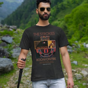 May include: A black t-shirt with a graphic design featuring the band The Strokes. The design includes the band's name, the album title "Room on Fire", and album release date "30.10.03".