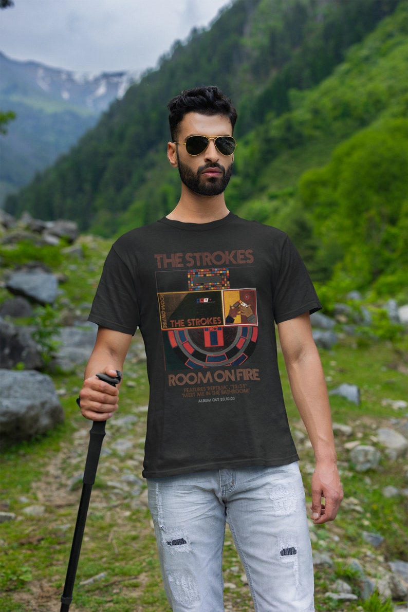 May include: A black t-shirt with a graphic design featuring the band The Strokes. The design includes the band's name, the album title "Room on Fire", and album release date "30.10.03".