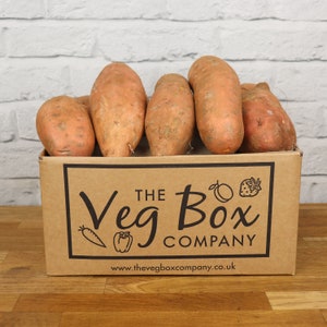 May include: A cardboard box filled with six sweet potatoes. The box is brown and has the text "The Veg Box Company" printed on it. The website address is also printed on the box: www.thevegboxcompany.co.uk.