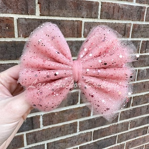May include: A large pink tulle bow with glitter accents. The bow is tied in a knot in the center.