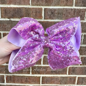May include: A large purple sequined bow with a lavender ribbon. The bow is made of small, iridescent sequins and is perfect for adding a touch of sparkle to any outfit.
