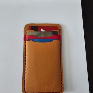 Op de afbeelding: Een bruinleren kaarthouder met rode stiksels. De kaarthouder heeft meerdere sleuven en bevat verschillende creditcards. De randen zijn netjes gestikt en het leer heeft een gladde afwerking. De kaarthouder is rechthoekig en ontworpen voor gemakkelijke toegang.