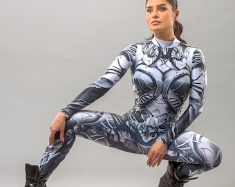 May include: A woman wearing a black and white printed jumpsuit with a high neck and long sleeves. She is posing with her legs crossed and her arms bent at the elbows. She is wearing black platform boots.
