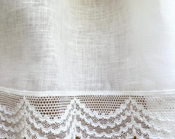 May include: Close-up of white linen fabric with a delicate lace trim. The lace features a scalloped edge and intricate openwork design. The fabric appears to be slightly translucent, with a subtle texture visible.