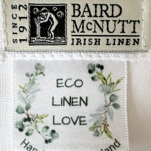 May include: Two fabric labels on white linen. The top label reads "BAIRD McNUTT IRISH LINEN SINCE 1912" with a black and white illustration. The bottom label says "ECO LINEN LOVE" with a floral design and "Handmade in Scotland".