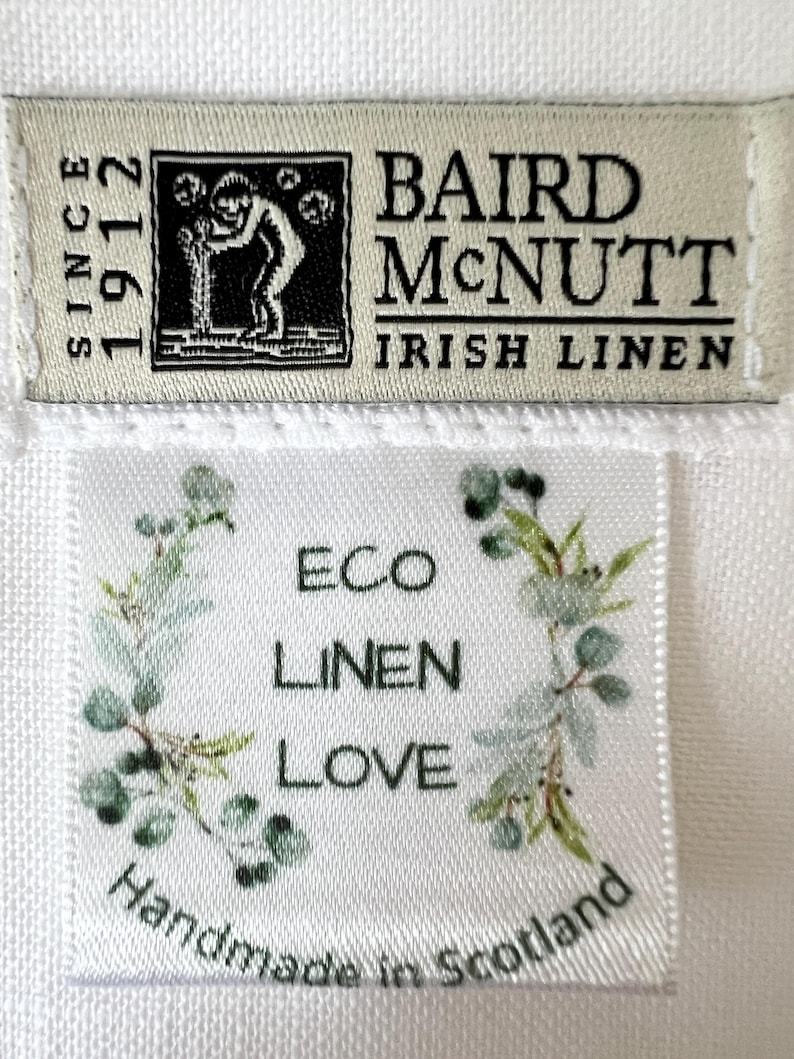 May include: Two fabric labels on white linen. The top label reads "BAIRD McNUTT IRISH LINEN SINCE 1912" with a black and white illustration. The bottom label says "ECO LINEN LOVE" with a floral design and "Handmade in Scotland".