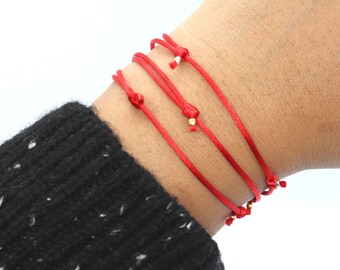 May include: Red string bracelets with gold beads on a person's wrist.