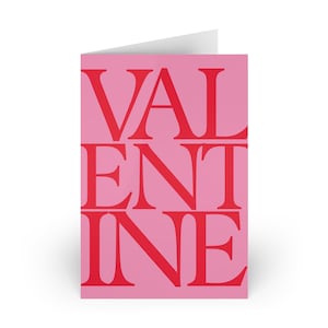 Può includere: Un biglietto di auguri piegato con sfondo rosa e la parola "VALENTINE" in grandi lettere maiuscole rosse. Il biglietto è bianco all'interno.