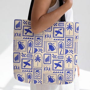 May include: Tote bag featuring a repeating pattern of blue illustrations on a cream background. The pattern includes birds, monkeys, palm trees, and other shapes. The bag has black handles.
