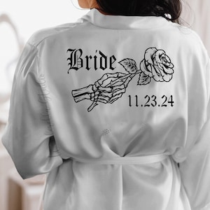 May include: White satin robe with a black skeleton hand holding a rose and the text "Bride" and "11.23.24" printed on the back.