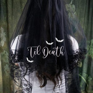 Peut inclure: Voile de mariée en tulle noir avec bordure en dentelle et le texte "Til Death" en blanc avec des silhouettes de chauves-souris.