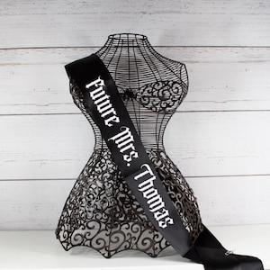 May include: Black satin sash with white text that reads "Future Mrs. Thomas".