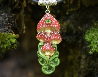 May include: A red and white mushroom pendant necklace with a green eye, set against a green mossy background. The necklace is made of polymer clay and features a silver chain.