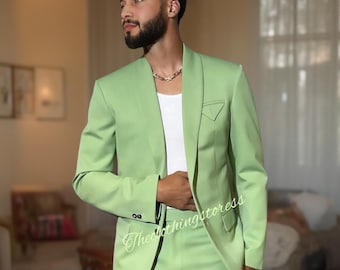 May include: A light green suit with a matching blazer and trousers. The blazer has a notched lapel and a small pocket detail. The person is wearing a white undershirt and a silver chain necklace. The text "Theclothingstores" is visible on the suit.